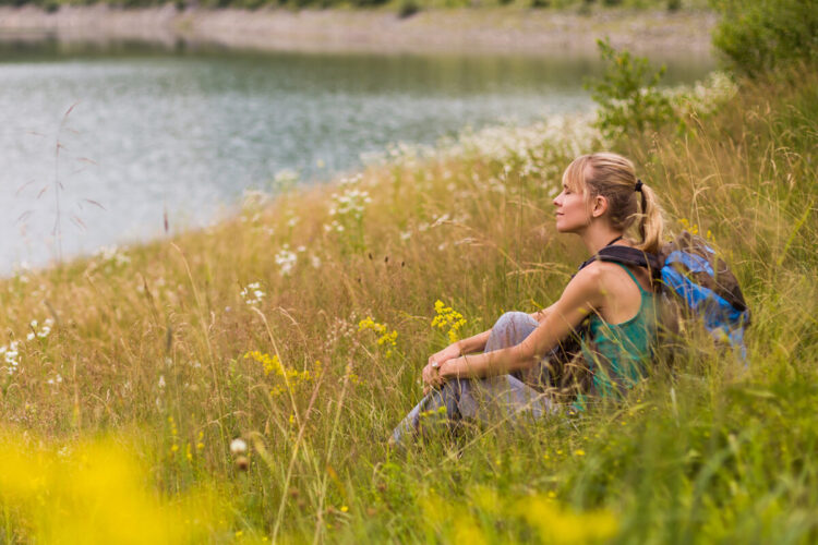 A woman sitting in tall grass near the water.